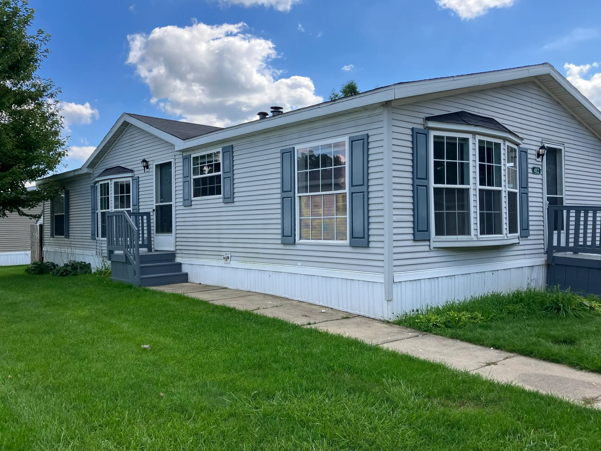 Daytime exterior shot of a modular home in Morrice Meadows, MI, showcasing a well-maintained lawn and surrounding landscape